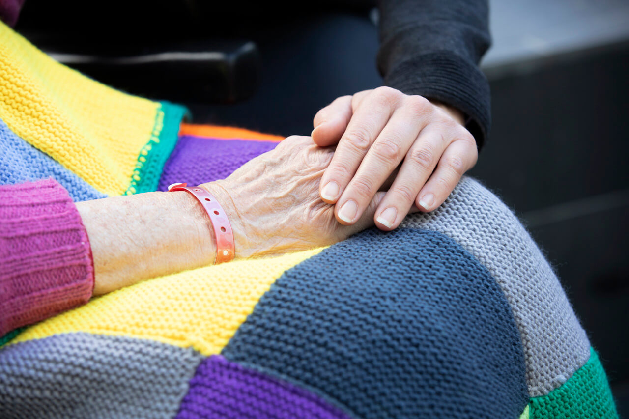 Nurse holding hand in comfort of elderly patient in aged care hospital